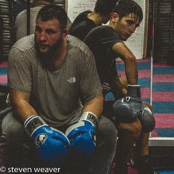Courtney sitting on a bench in the gym with blue gloves on, between rounds